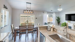 A modern kitchen with granite countertops, a stainless steel sink, and a dining area with wooden chairs and a table. - Bakersfield Home w/ Pool Table, Cornhole + More! (Bakersfield)