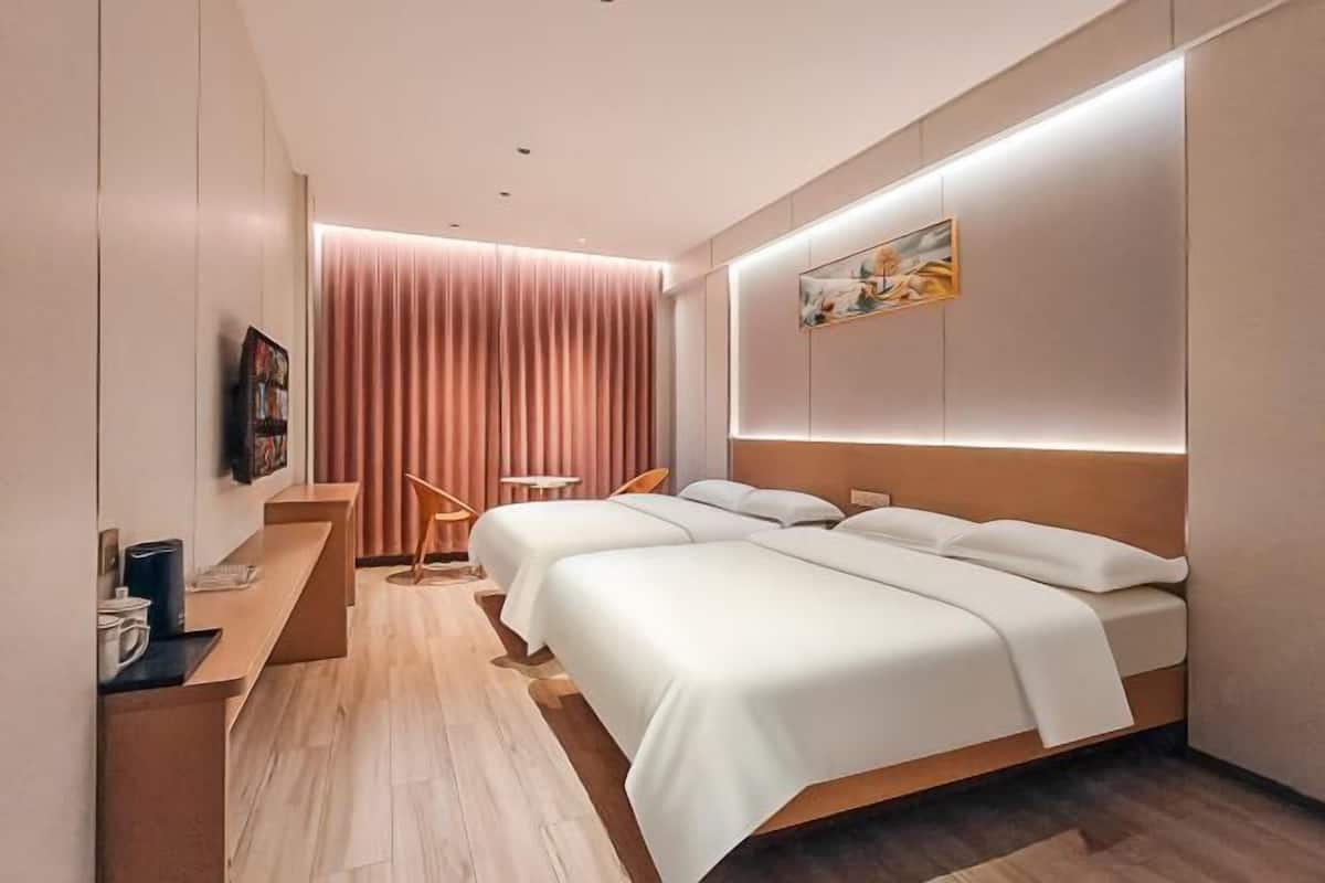 Ein modernes Hotelzimmer mit Holzboden, einem Schreibtisch mit Stuhl, zwei Betten, einem an der Wand befestigten Fernseher und einem großen Fenster mit Vorhängen.