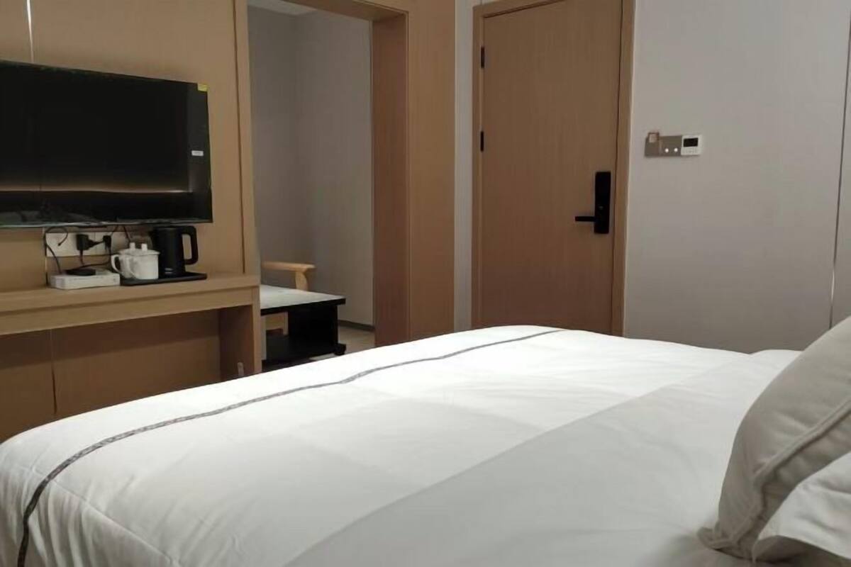 Ein Hotelzimmer mit einem Bett, einem an der Wand montierten Fernseher, einer Kaffeemaschine und einer Tür.