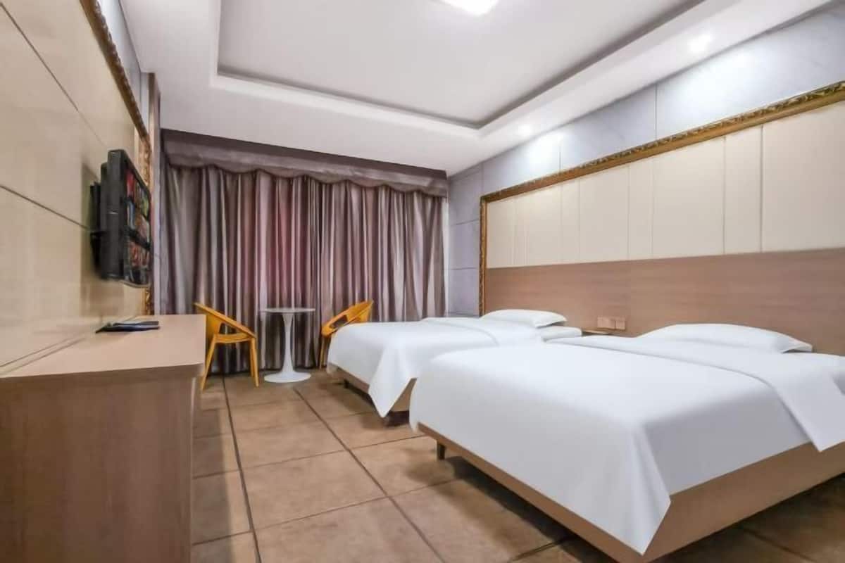 Ein Hotelzimmer mit zwei Betten, einem Schreibtisch, einem Stuhl, einem Fernseher und einem Vorhang.