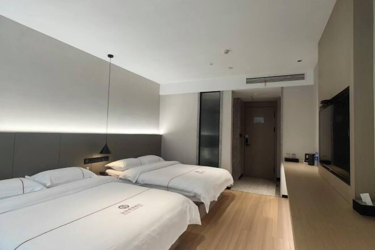 A modern hotel room with two beds, a large mirror, and a TV.