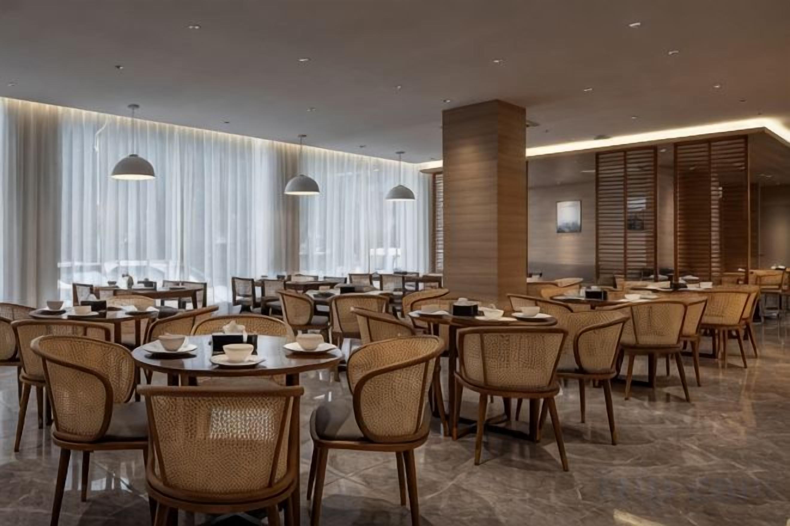 A modern dining area with round tables, wicker chairs, and pendant lighting.