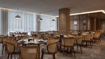 A modern dining area with round tables, wicker chairs, and pendant lighting.