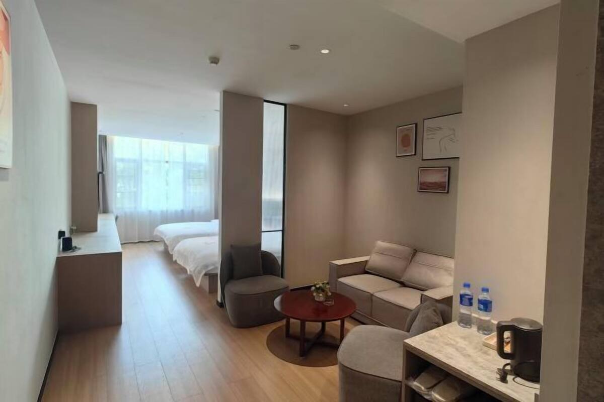 A modern hotel room with a bed, a sofa, a small table, and a coffee machine.