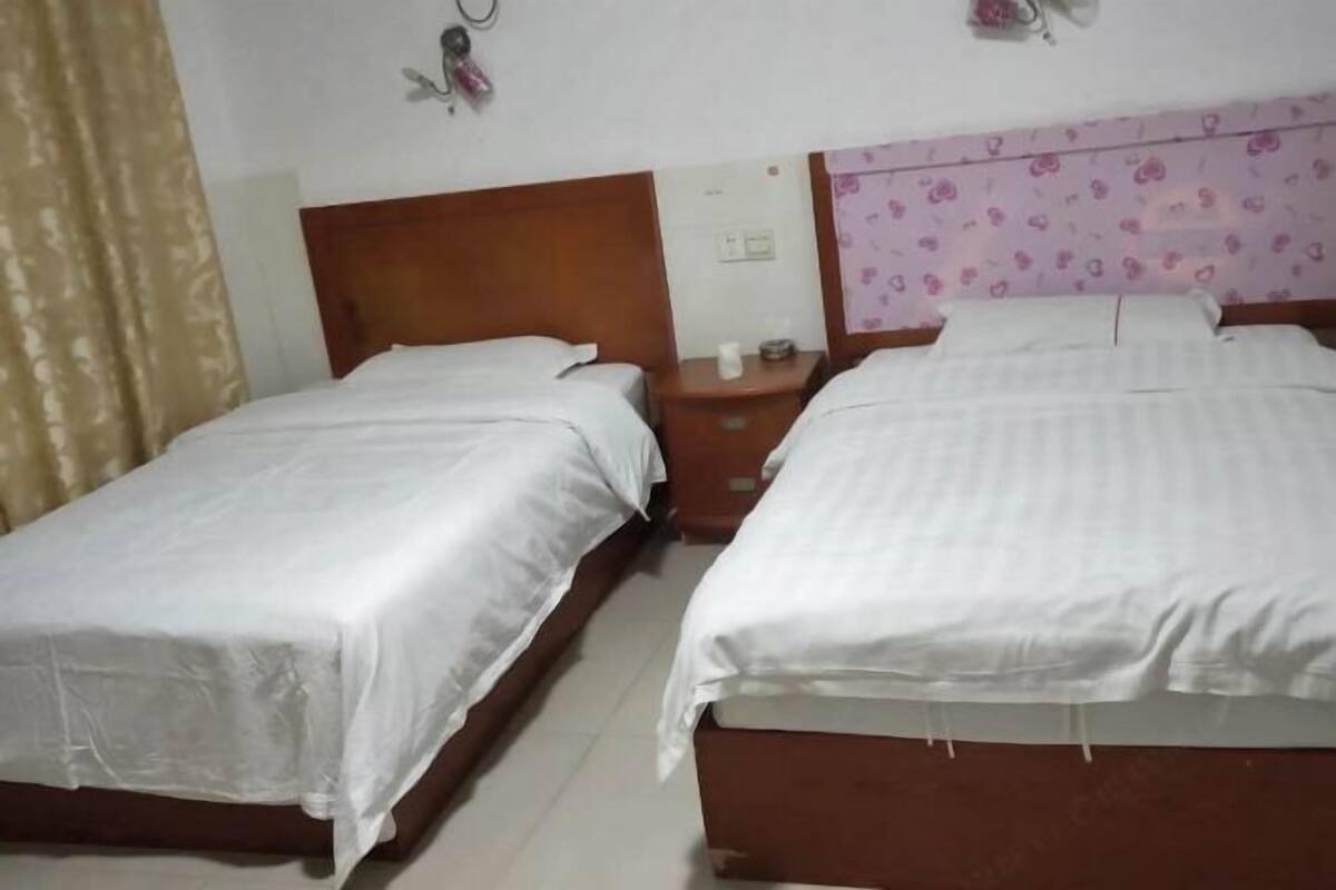 Dos camas individuales con cabeceros de madera, una mesita de noche con lámpara, y una pared con estampado floral.