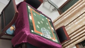 Habitació amb un llit cobert per un llençol morat, una catifes amb dibuixos verds i taronja, i una finestra amb cortines beix.