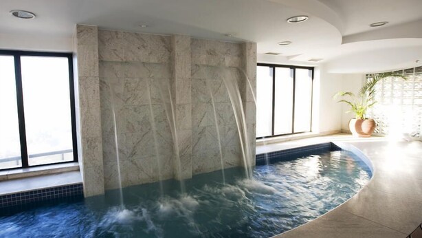A spa area with a hot tub, marble walls, and large windows. - Flat Hotel GRU SL Guarulhos (Guarulhos)