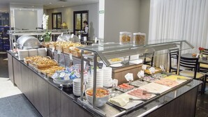 A buffet setup with various food items, including bread, meats, and salads, in a modern hotel setting. - Flat Hotel GRU SL Guarulhos (Guarulhos)