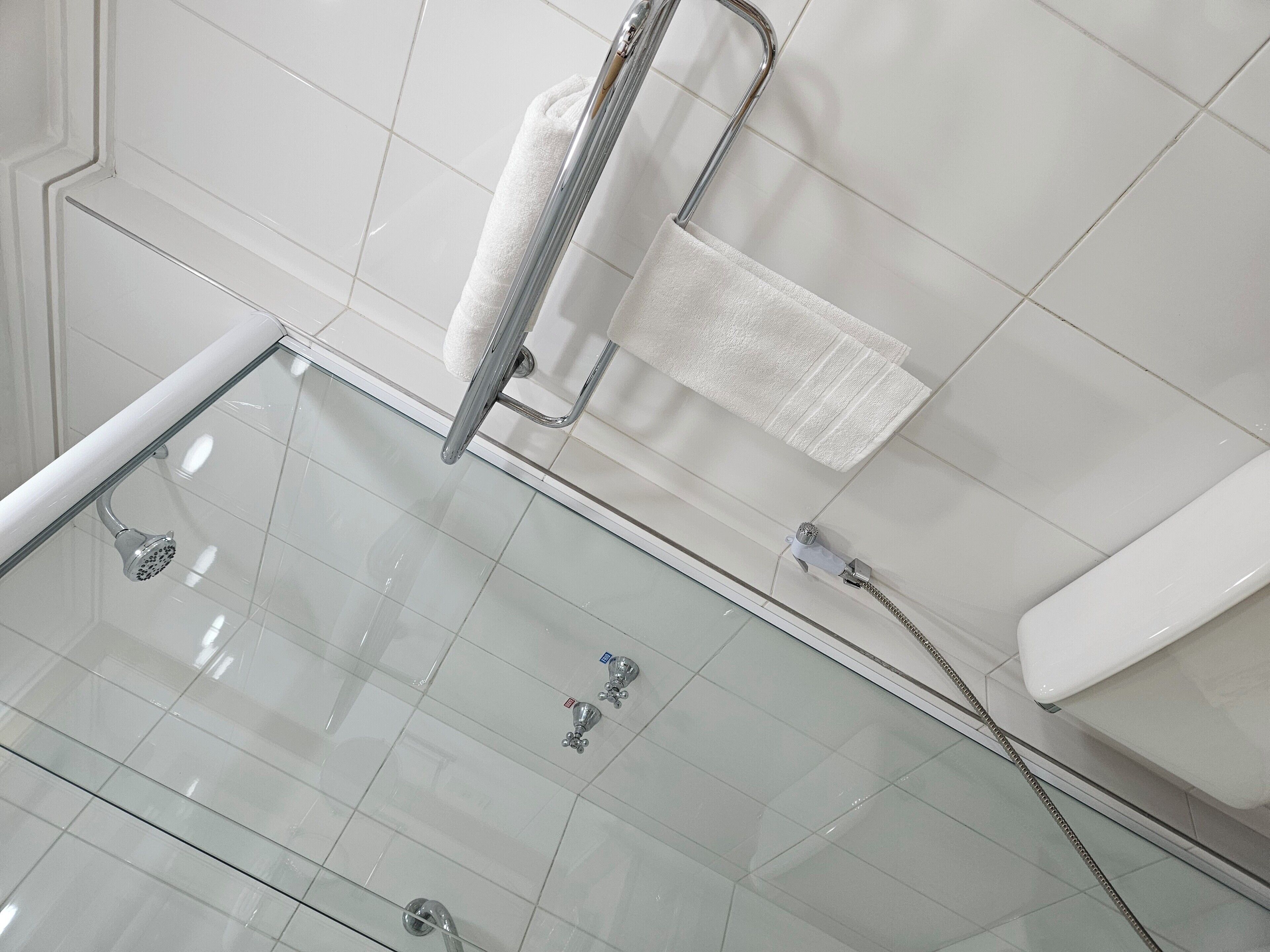 A modern bathroom with a glass shower enclosure, a white towel rack, and a white toilet.