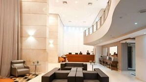 A modern lobby with a reception desk, seating area, and a high ceiling with recessed lighting. - Flat Hotel GRU SL Guarulhos (Guarulhos)