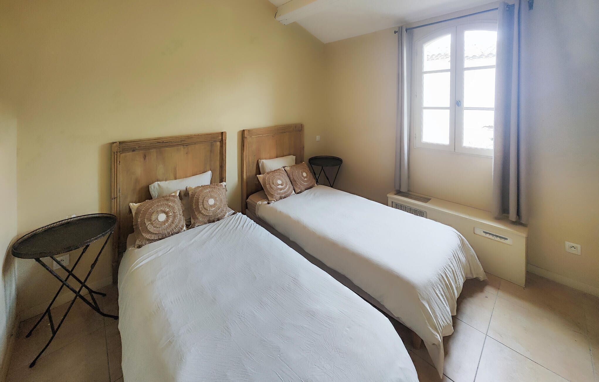 Habitación de hotel con dos camas individuales, una mesita, una silla y una ventana con cortinas.