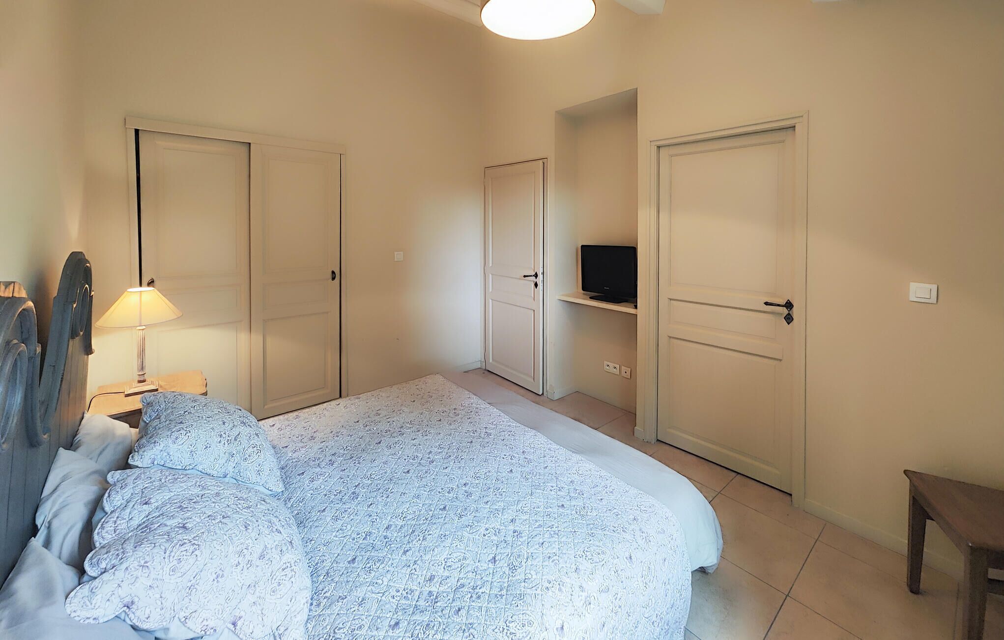 Een slaapkamer met een bed, een televisie op een plank en twee deuren.