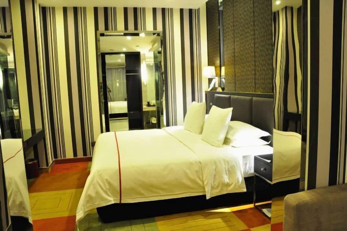 A hotel room with a large bed, a bedside table, a mirror, and striped curtains.