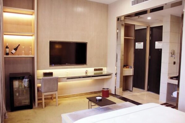 Une chambre d’hôtel comprenant un lit, un bureau avec une chaise, une télévision, un minibar et une salle de bain avec douche et toilettes.