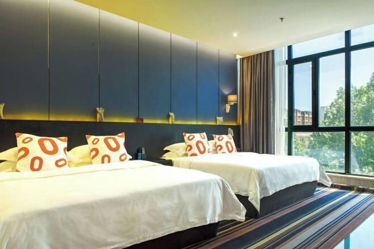 A hotel room with two beds, a large window, and a view of greenery outside.
