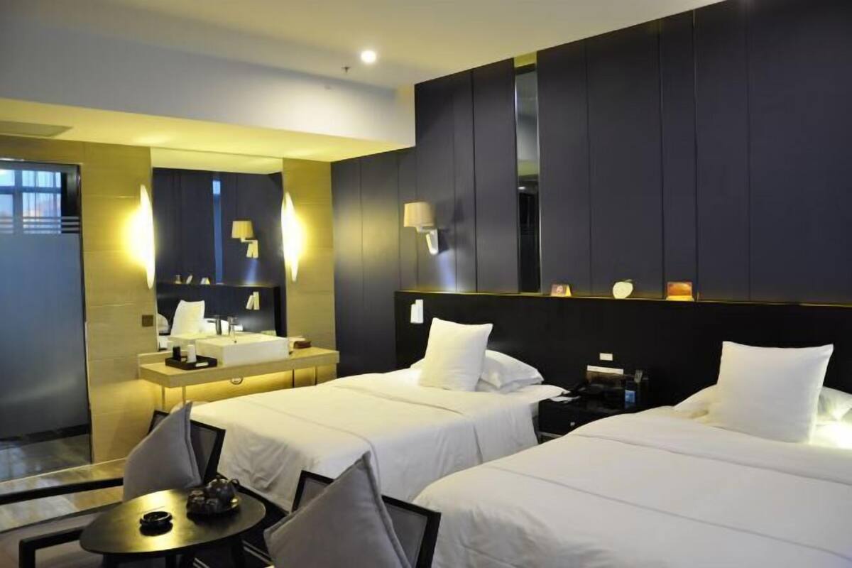 A hotel room with two beds, a desk, a chair, a small table, and a mirror.