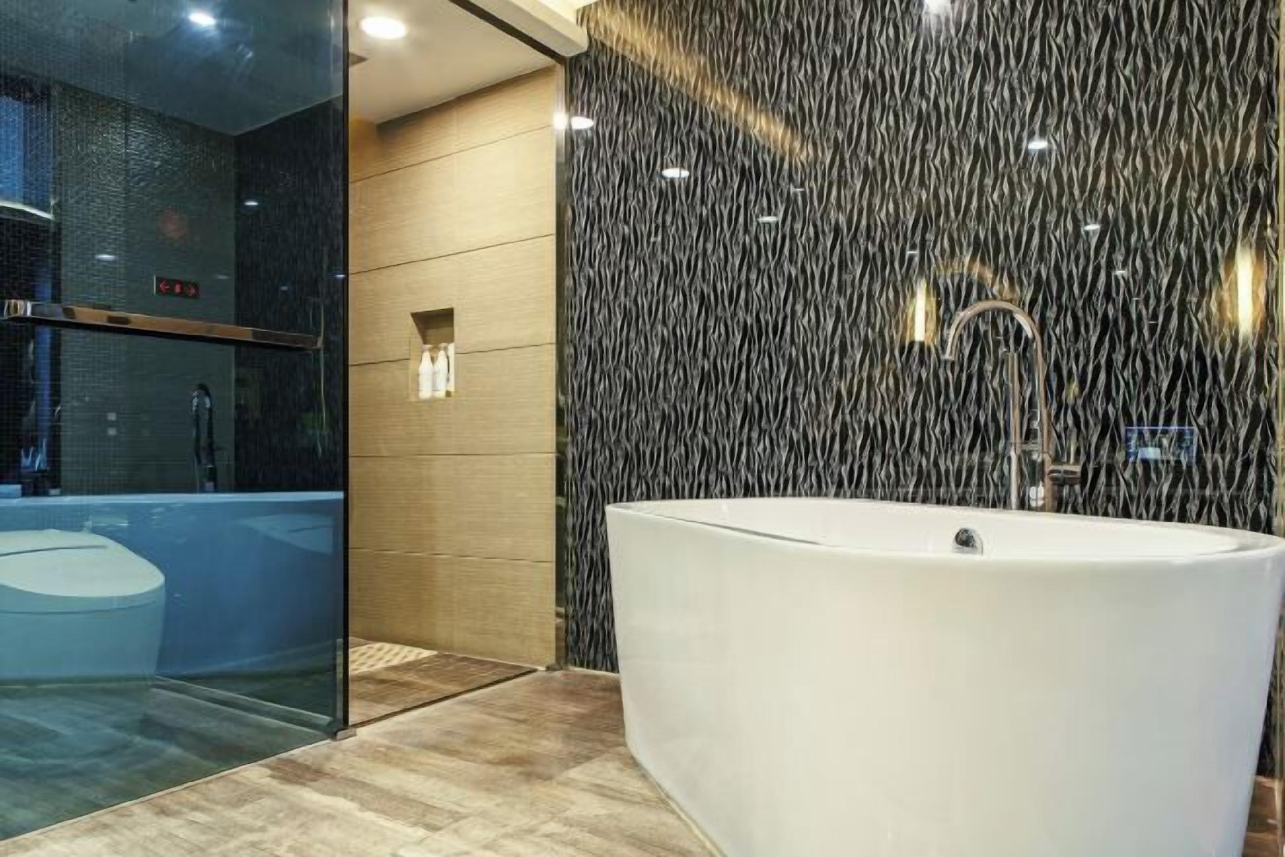 Une salle de bain moderne avec une baignoire sur pieds, une douche à l’italienne avec des parois en verre et un mur à texture.