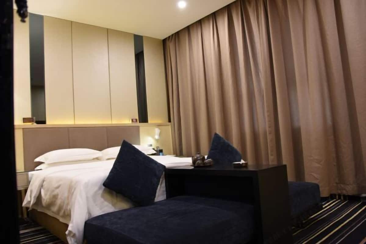 A hotel room with a bed, a desk, and a chair. There is a window with curtains.