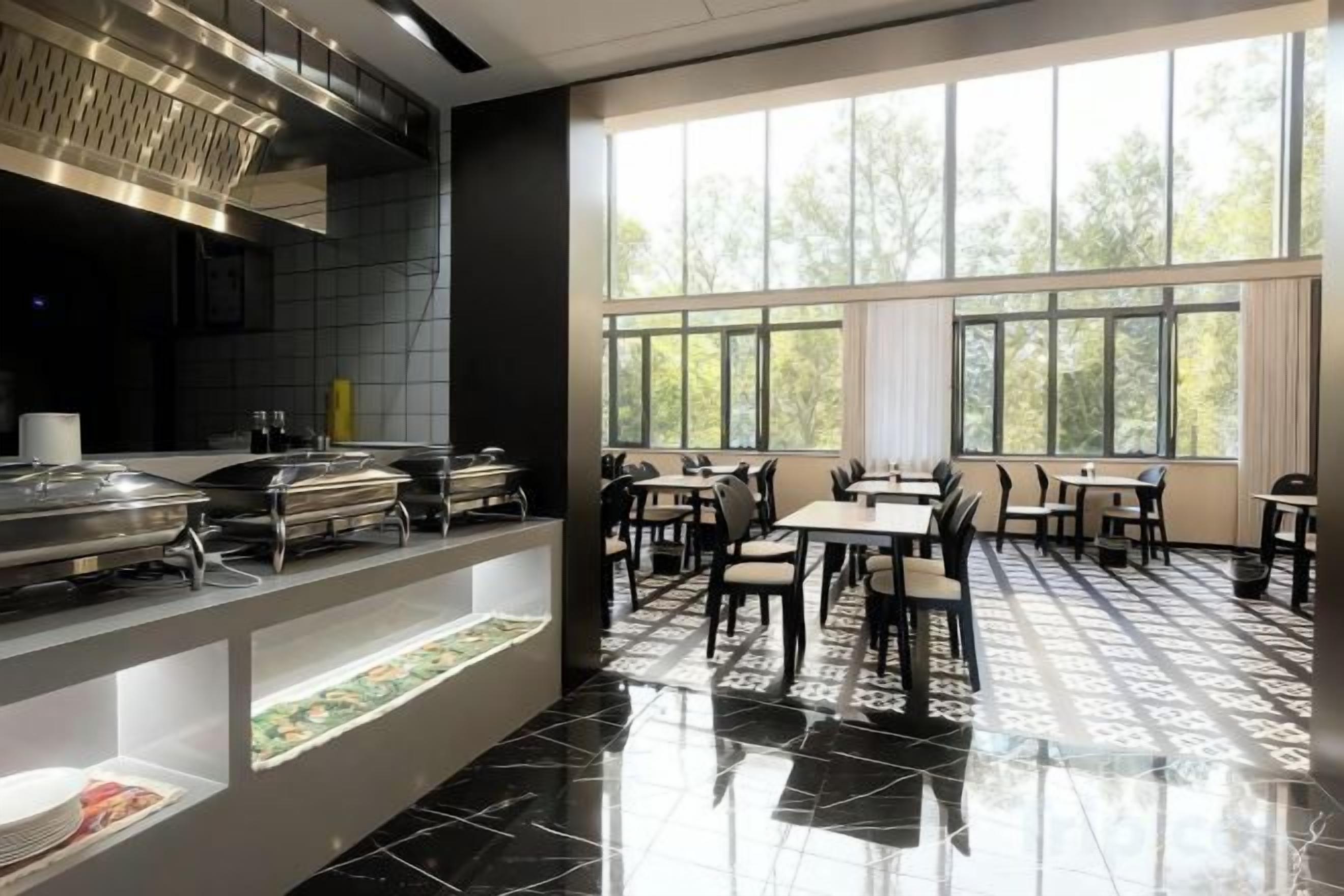 A restaurant with a buffet setup, large windows, and a tiled floor.