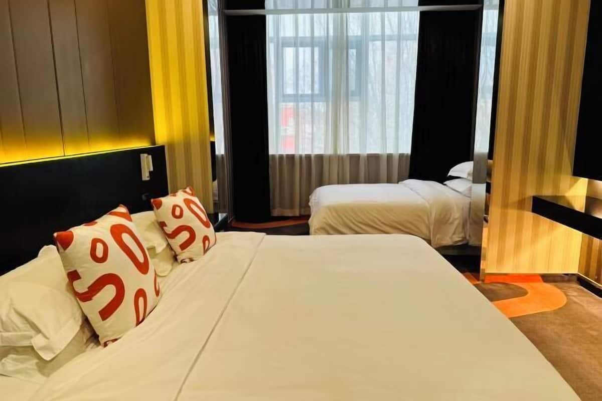 A hotel room with a bed, two pillows, a window with curtains, and a wooden headboard.