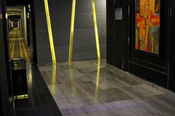 Un couloir avec un sol à carreaux, un mur à motifs et un tableau accroché sur le côté droit.