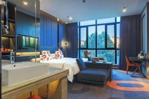 Una habitación de hotel moderna con una cama grande, un escritorio y vistas al exterior a través de amplios ventanales.