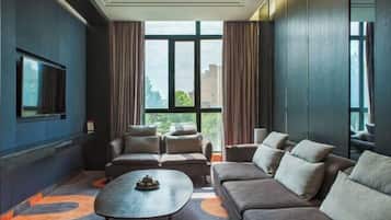 A modern hotel room with a large window, a flat-screen TV, a sofa, a coffee table, and a patterned carpet.
