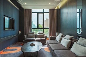 Una habitación de hotel moderna con un ventanal grande, un televisor de pantalla plana, un sofá, una mesita de café y una alfombra estampada.