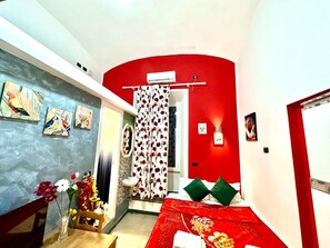 A room with a red accent wall, a bed with a red and white floral bedspread, a white air conditioning unit, a shower curtain with a floral pattern, and a small table with a vase of flowers. - B&B Termini Colosseo Suite (Rome)