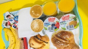 Una bandeja con alimentos para el desayuno, incluyendo plátanos, Nutella, un croissant, un muffin y un envase de yogur.