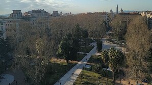 Un parque con senderos, árboles y edificios al fondo.