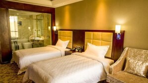 A hotel room with two beds, a sofa, a glass shower enclosure, and a wooden headboard.