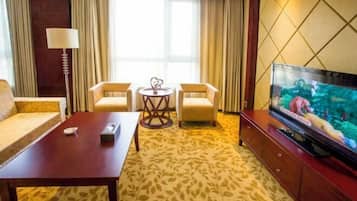 Een hotelkamer met een bank, twee fauteuils, een klein rond tafeltje, een televisie op een houten kast en een kamerbreed tapijt met dessin.