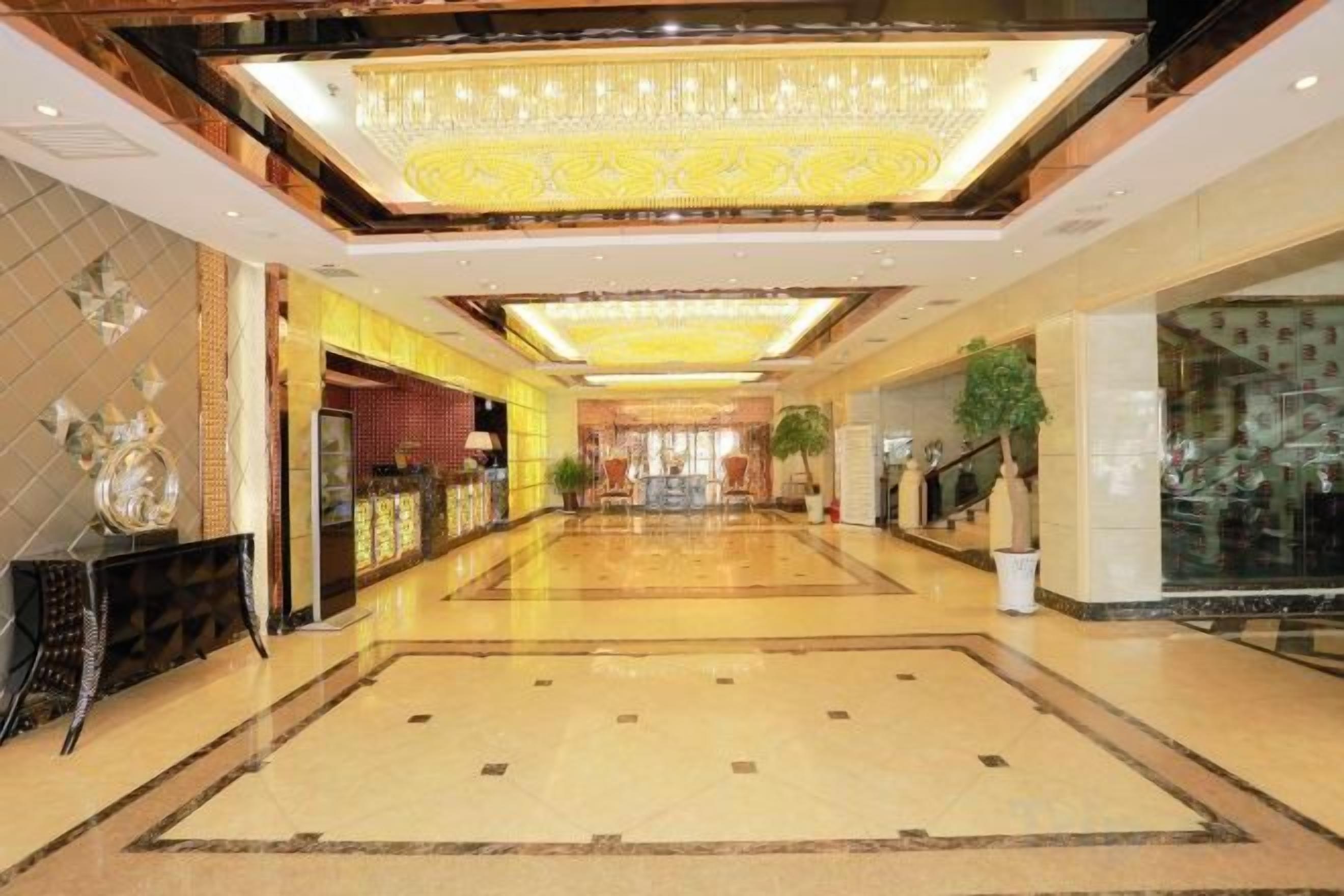 Un hall d’hôtel avec un long couloir, un comptoir d’accueil et un lustre.