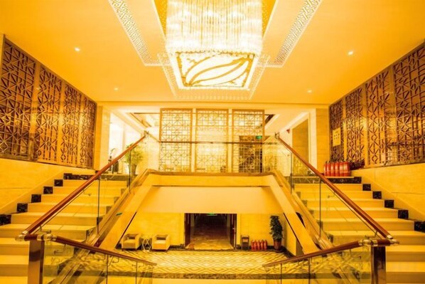 A hotel lobby with a grand staircase, a chandelier, and patterned walls.