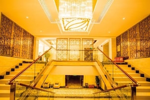 Un vestíbulo de hotel con una imponente escalera, un candelabro y paredes con diseños.
