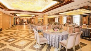 A spacious banquet hall with round tables and chairs, a patterned floor, and a large chandelier.