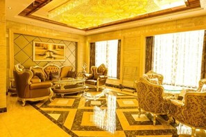 Un hall d’entrée luxueux avec un plafond haut, un décor orné et un grand lustre. On y trouve plusieurs espaces de détente avec des canapés et des fauteuils confortables.