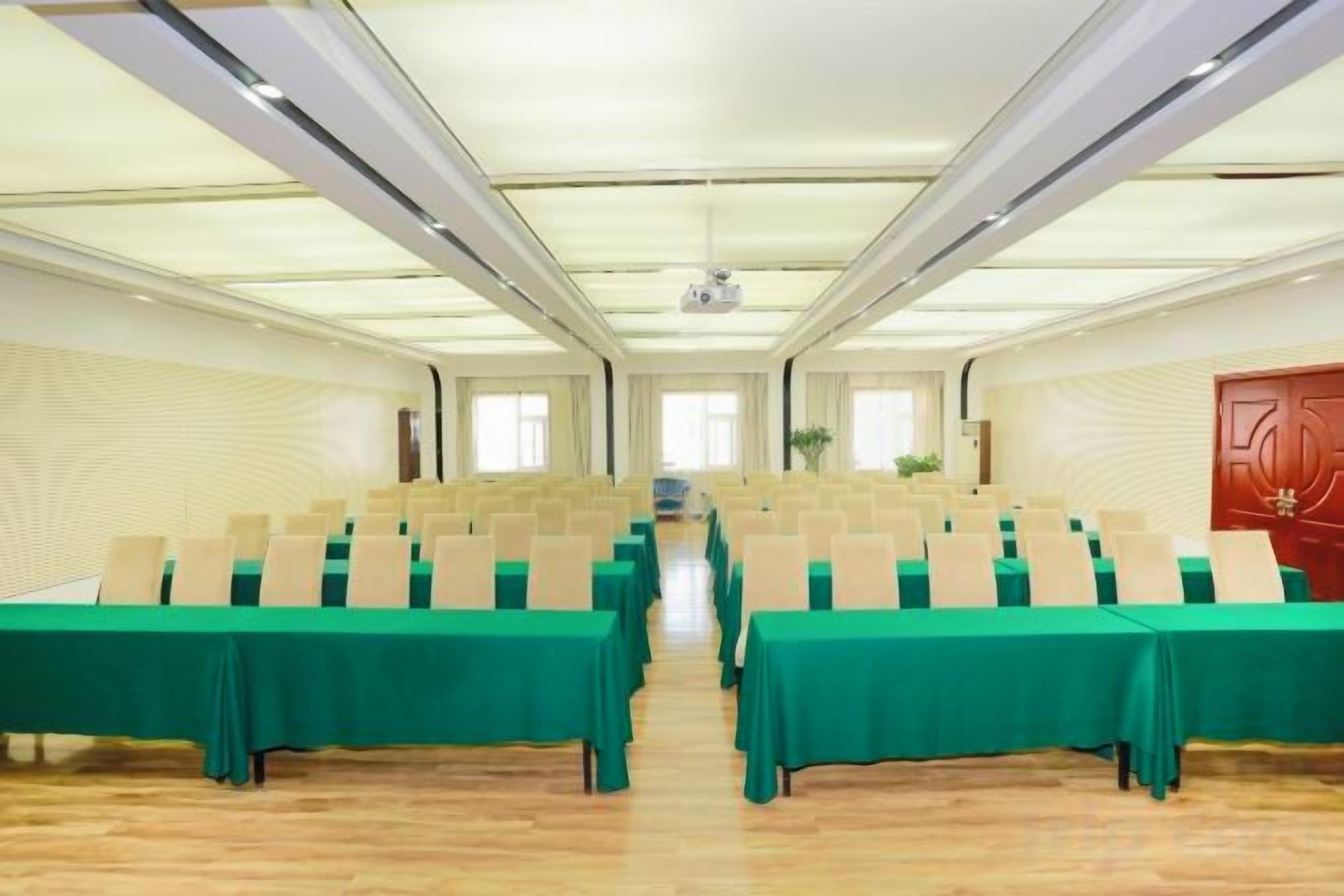 Un salón de conferencias con filas de mesas, un proyector y una puerta roja.