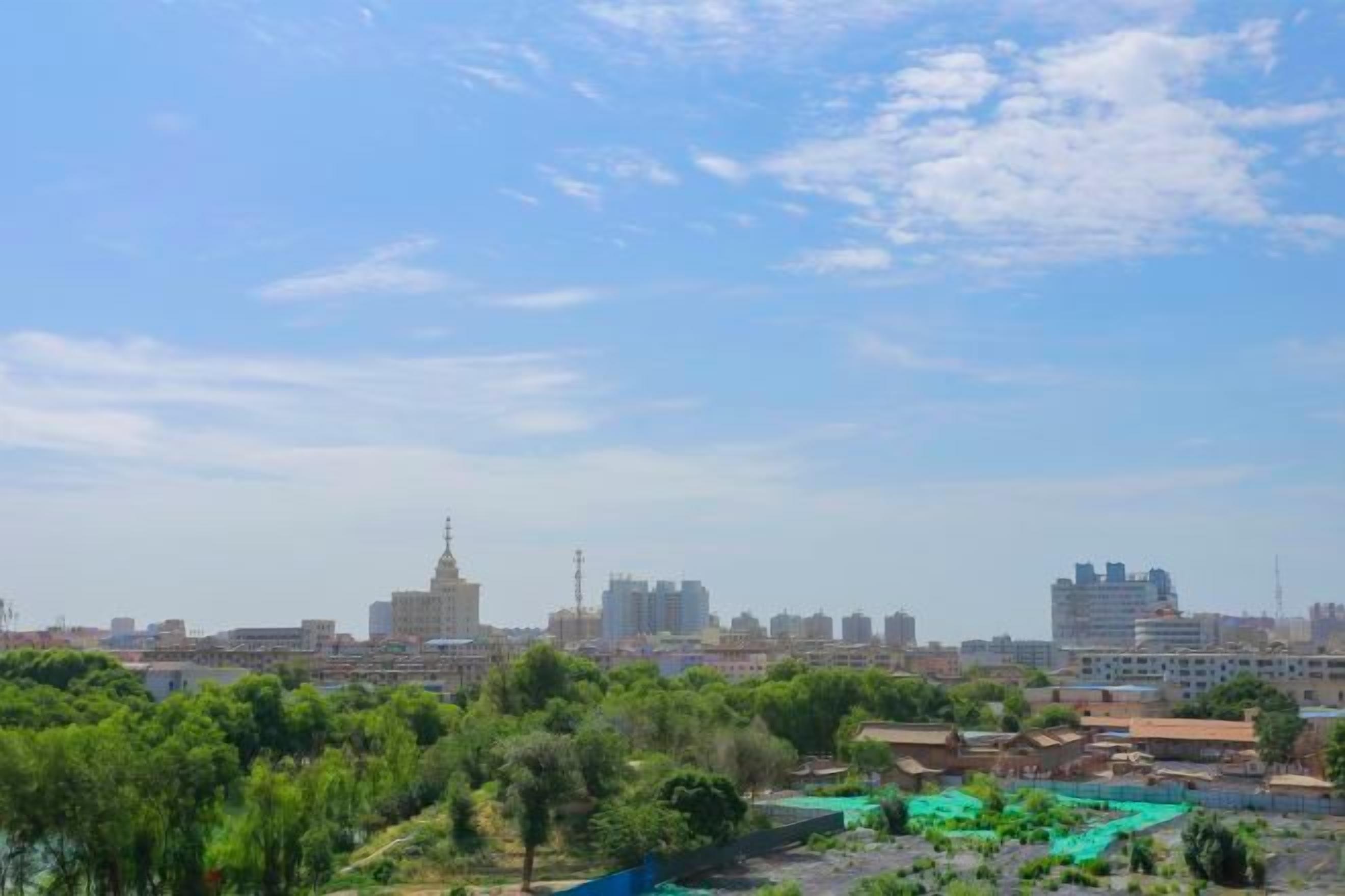 A cityscape with a prominent tower, greenery, and a clear sky.
