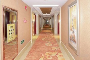Un pasillo de hotel con alfombra estampada, obras de arte enmarcadas en las paredes y un cartel a la izquierda.