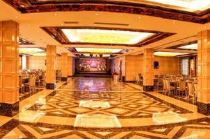 Un amplio vestíbulo de hotel con un escenario central, varias zonas de estar y un suelo estampado.