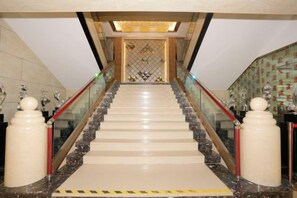 A grand staircase with marble steps and glass railings, leading to a decorative area with a patterned wall and a chandelier. - Xiaolajiao Hotel (Zhangye Jinzuo) (Zhangye)