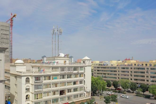 Un edificio de varios pisos con balcones, un estacionamiento y una grúa de construcción al fondo.
