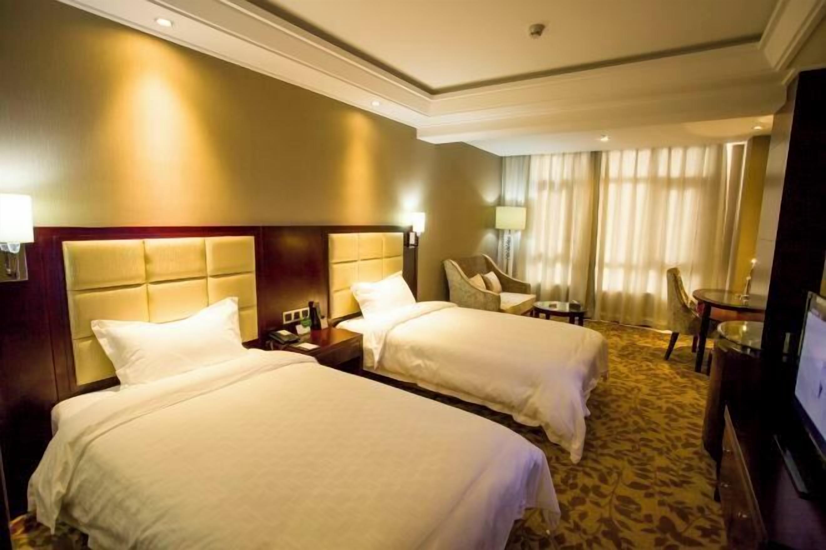 A hotel room with two beds, a television, a desk, and a chair.