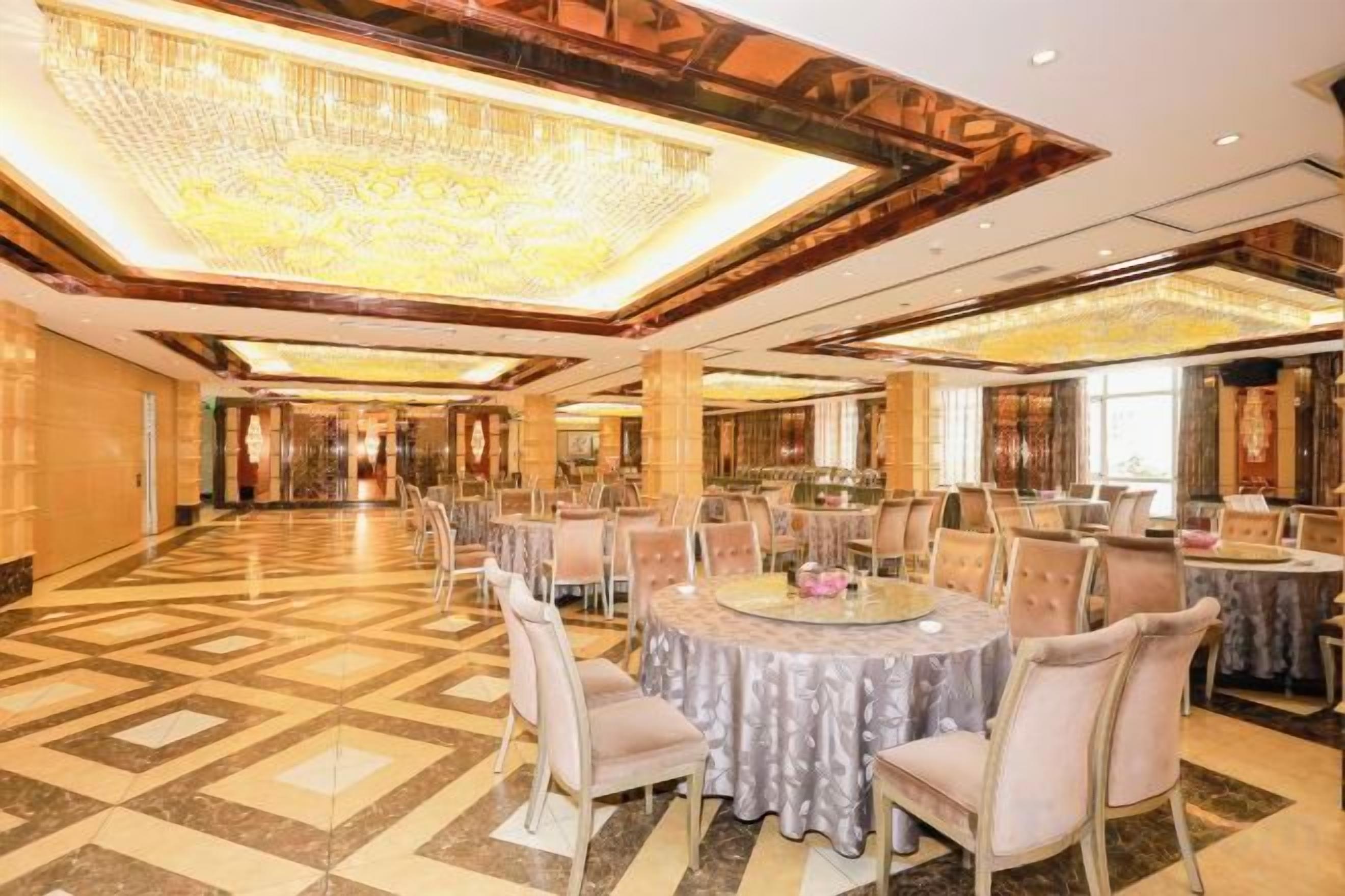A spacious banquet hall with round tables and chairs, a large chandelier, and a polished floor.