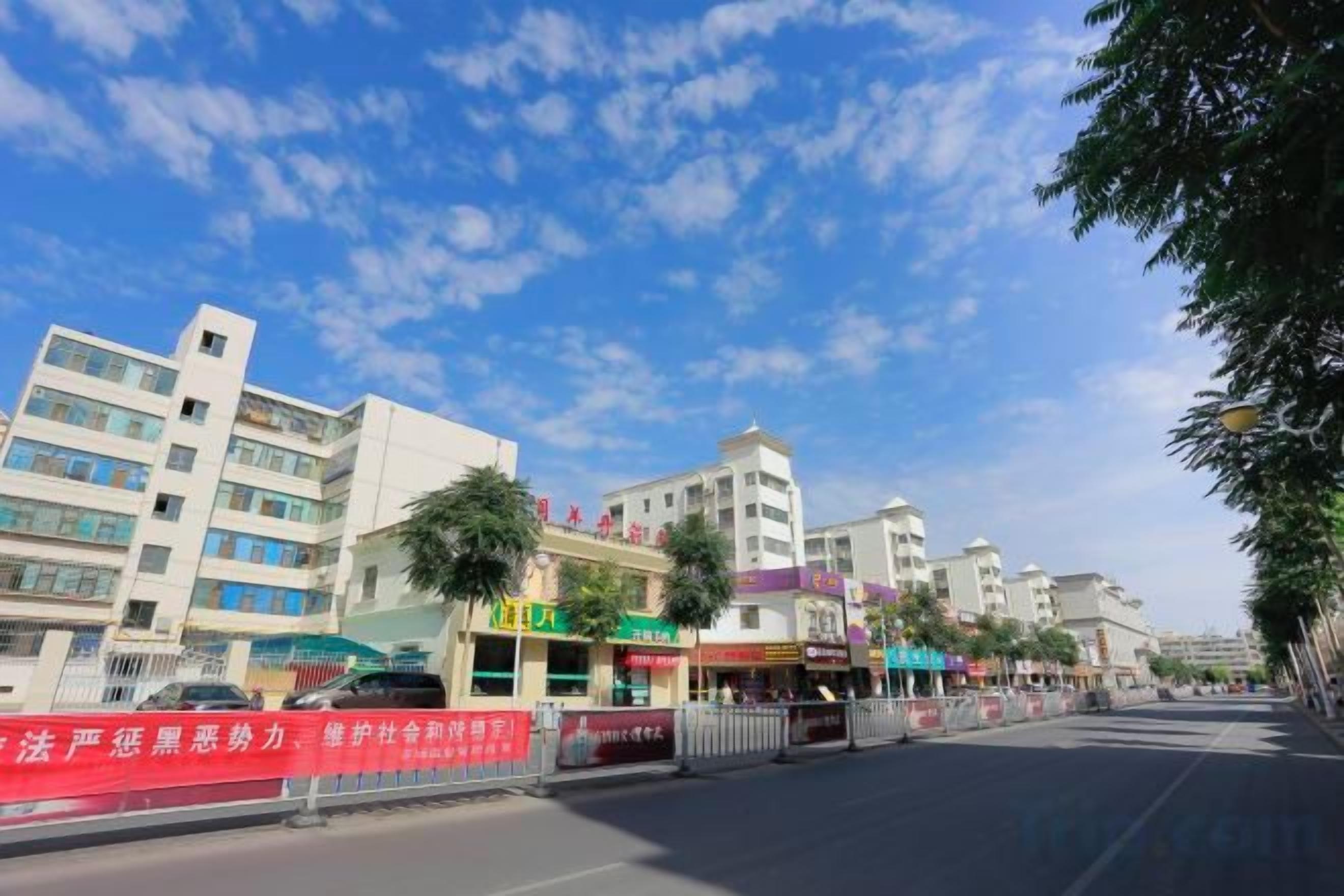 A multi-story building with commercial establishments on the ground floor, a clear sky, and a pedestrian walkway.