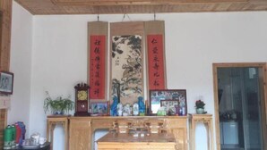 A traditional room with wooden ceiling and walls, a wooden cabinet with various items, and three vertical banners with Chinese characters. - Huiyun Homestay, Yuli Ancient Town (Fuliang)