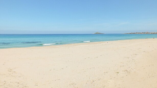 Ein breiter Sandstrand mit klarem, blauem Wasser und einer entfernten Insel.