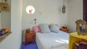 Ein Schlafzimmer mit einem Bett, Nachttischen, einer Wandlampe, einer Pendelleuchte und einem kleinen Regal mit Gegenständen.